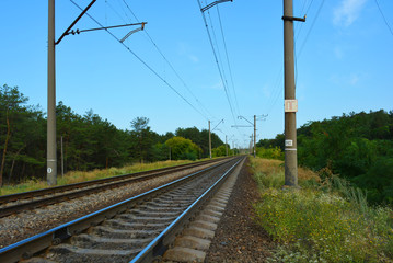 Fototapeta na wymiar Railway track, railway and electric power lines for electric vehicles, electric trains lying along coniferous forests with blue sky, clouds. Infrastructure of Severny housing estate, Dnipro, Ukraine.