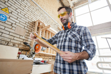 Low angle portrait o mature carpenter holding wooden board in joinery workshop