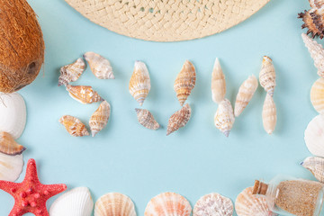 The word sun written in shells on blue background. Around the word are frame from seashells, starfish, sand bottle and coconut. Flat lay of vacation concept