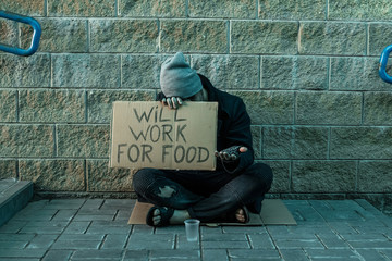 A man, homeless, a man asks for alms on the street with a sign will work for food. Concept of...