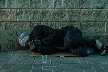A man, homeless, a man sleeping on a cold floor in the street with a Help sign. Concept of a...