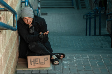 A man, homeless, a man sleeping on a cold floor in the street with a Help sign. Concept of a homeless person, social problem, addict, poverty, despair.