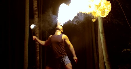 Fantastic fire show muscular man in the dark spits fire