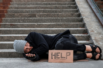 A man, homeless, a man sleeping on a cold floor in the street with a Help sign. Concept of a homeless person, social problem, addict, poverty, despair.