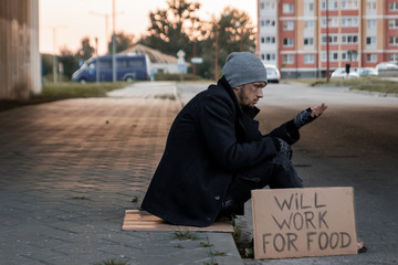A man, homeless, a man asks for alms on the street with a sign will work for food. Concept of a...