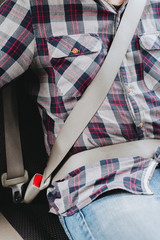 Photo of man in plaid shirt sitting in a car putting on seat belt