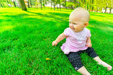 Little girl sitting on green grass, close up.