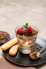 Classic tiramisu dessert portion with blueberries and raspberries in a glass cup on concrete background