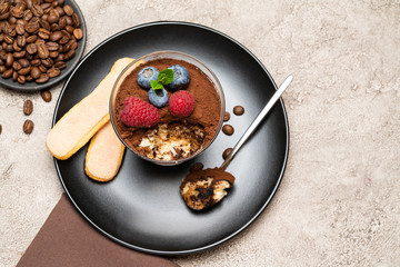Classic tiramisu dessert portion with blueberries and raspberries in a glass cup on concrete background