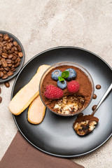 Classic tiramisu dessert portion with blueberries and raspberries in a glass cup on concrete background