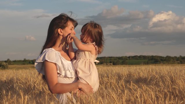 mother walks with the baby in the field hold spikelets with wheat in hand. little daughter kisses mom on wheat field. happy family travels. baby in the arms of mom. happy family concept.