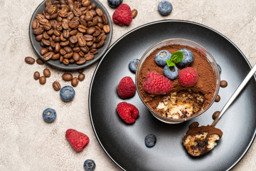 Classic tiramisu dessert portion with blueberries and raspberries in a glass cup on concrete background