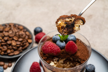 Classic tiramisu dessert portion with blueberries and raspberries in a glass cup on concrete background