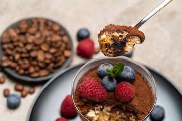 Classic tiramisu dessert portion with blueberries and raspberries in a glass cup on concrete background
