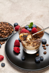 Classic tiramisu dessert portion with blueberries and raspberries in a glass cup on concrete background