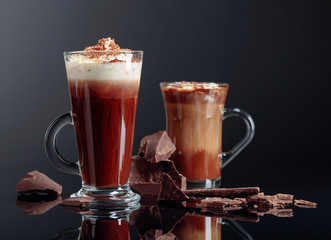 Hot chocolate with whipped cream and pieces of dark chocolate on a black background.