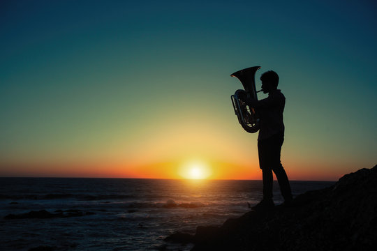 Silhouette of musician with tuba on the beach during amazing sunset.
