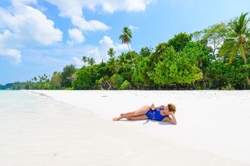 Woman using smart phone relaxing on white sand beach, real people traveling around the world. Indonesia tropical destination, lifestyle sharing social media concept.