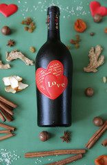 Flat lay. Still life with a bottle of wine with a red heart on a bottle with an inscription about love on a green background with spices and dried fruits for mulled wine Christmas Valentine's Day Love