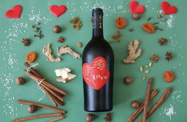 Flat lay. Still life with a bottle of wine with a red heart on a bottle with an inscription about love on a green background with spices and dried fruits for mulled wine Christmas Valentine's Day Love