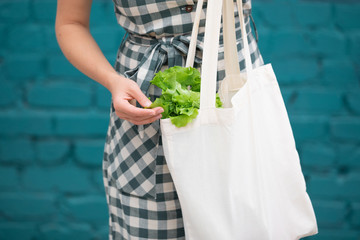 Female hand with cotton eco bag on wooden grey background. Zero waste concept