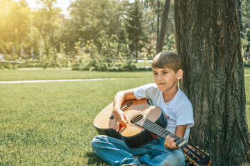 A boy with a guitar sits under a tree, sings songs and enjoys nature.
