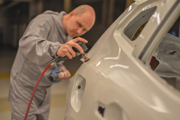 A worker in the painting shop of a car body, sanding painted items