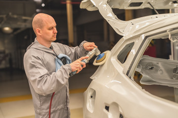 Employee in the shop painting the car body polishes painted body parts