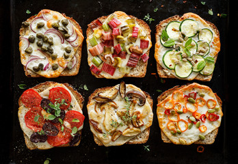 Vegetarian toast with grilled slices of bread with the addition of cheese and various vegetable toppings on a black background, top view
