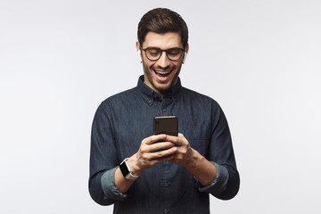 Young man laughing as he is looking at phone, isolated on gray background
