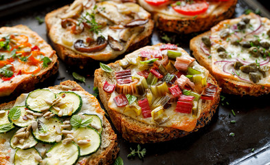 Vegetarian toast with grilled slices of bread with the addition of cheese and various vegetable toppings on a black background, close-up