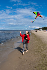 A teenage girl launches a kite on the shore of the Baltic Sea on the beach. A girl runs, and a kite flies after her. The concept is the hope for a happy future, the fulfillment of dreams, freedom.