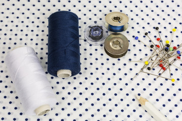 assortment of sewing accessories: thread in blue and white with bobbins, round-head needles and marking pencil