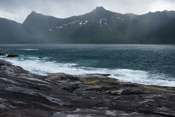 Beautiful nature landscape in North. Scenic outdoors view. Ocean with waves and mountains. Big dark stones. Dramatic storm clouds. Extreme weather, rain and wind. Explore Norway, summer adventure