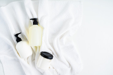 Set of Bottles with organic body care cosmetic products on white fluffy towels on a light background. Concept of SPA branding mock-up.