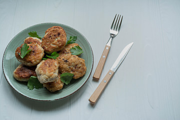 Cutlets with herbs served on a plate on a white wooden background.