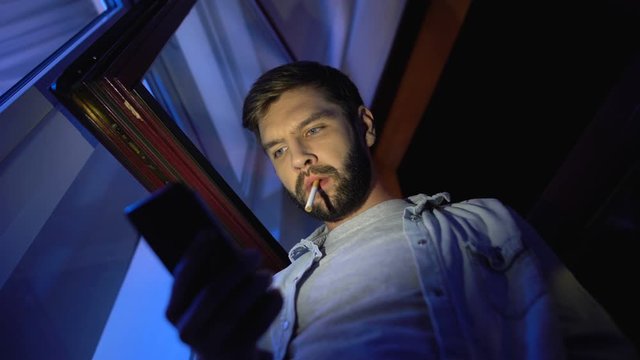 Bottom view of suspicious man chatting smartphone, smoking cigarette at night