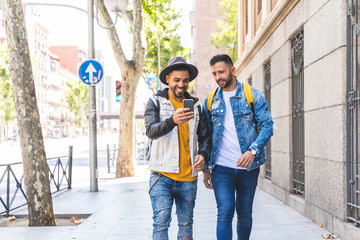 Two Male Friends Walking Together in the Street While Using Cell Phone.