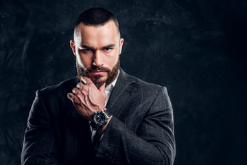 Serious sceptical buisnessman with beard and in dark clothing is standing at dark photo studio.