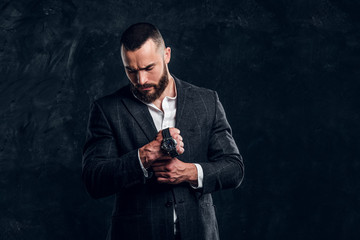 Sucessful serious man is posing for photographer with watch on his fist on the dark background.