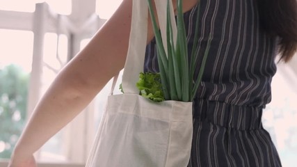 Young woman with reusable cotton Eco produce bag coming home after shopping fruits and vegetables. Zero waste lifestyle concept. Ecology. Slow motion