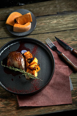 Roasted duck leg with confit pumpkin, closeup. Horizontal top view, top shot. Copy space, wooden background, low key