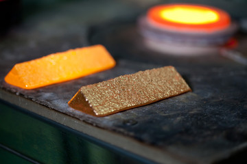 closeup picture of ingots of melt gold, hot shiny metal bars on table and fire furnace on background