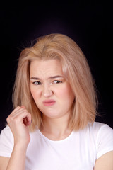 Portrait of a young blonde woman in a white T-shirt on a black background looking contemptuously...
