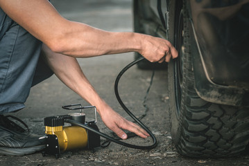 Driver is pumping the car wheel with a car pump.