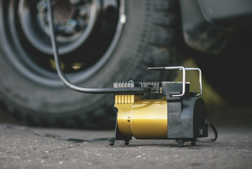 Car wheel and a air pump on the asphalt road close up background.