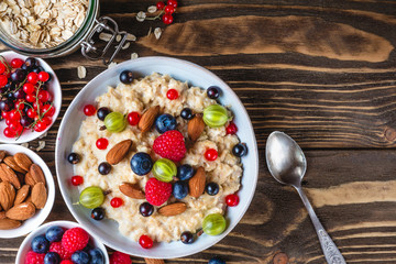 oatmeal porridge with fresh berries and nuts in a bowl on rustic wooden background for healthy diet breakfast. top view