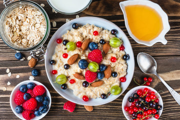 healthy breakfast. bowl of oatmeal porridge with berries, nuts, honey and glass of milk on rustic wooden table