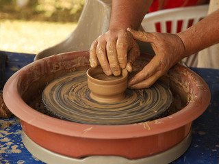 Hands of a potter sculpt clay dishes on a pottery wheel. Folk craft for making dishes. Creation of a ceramic product. Teaching ancient craft. Utensils for everyday life. History of folk art.