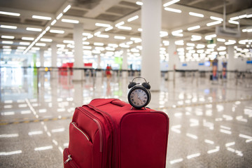 Time to travel or travel delay concept. Black Alarm clock on red suitcase. Abstract photo.